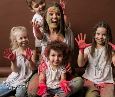 A happy group of children and woman covered in colorful powder, all smiles and joy.