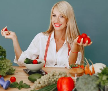 Healthy lifestyle concept with woman holding tomatoes and surrounded by fresh vegetables in a studio setting.